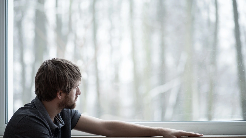 Uomo che guarda dalla finestra con problemi di depressione