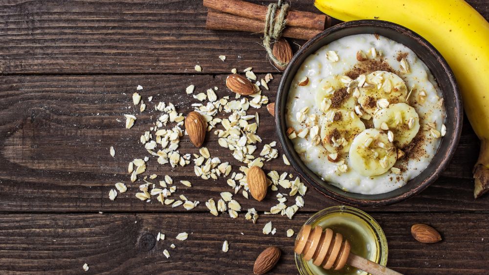 Una ciotola di porridge decorata con fette di banana, mandorle tritate, avena e una spolverata di cannella